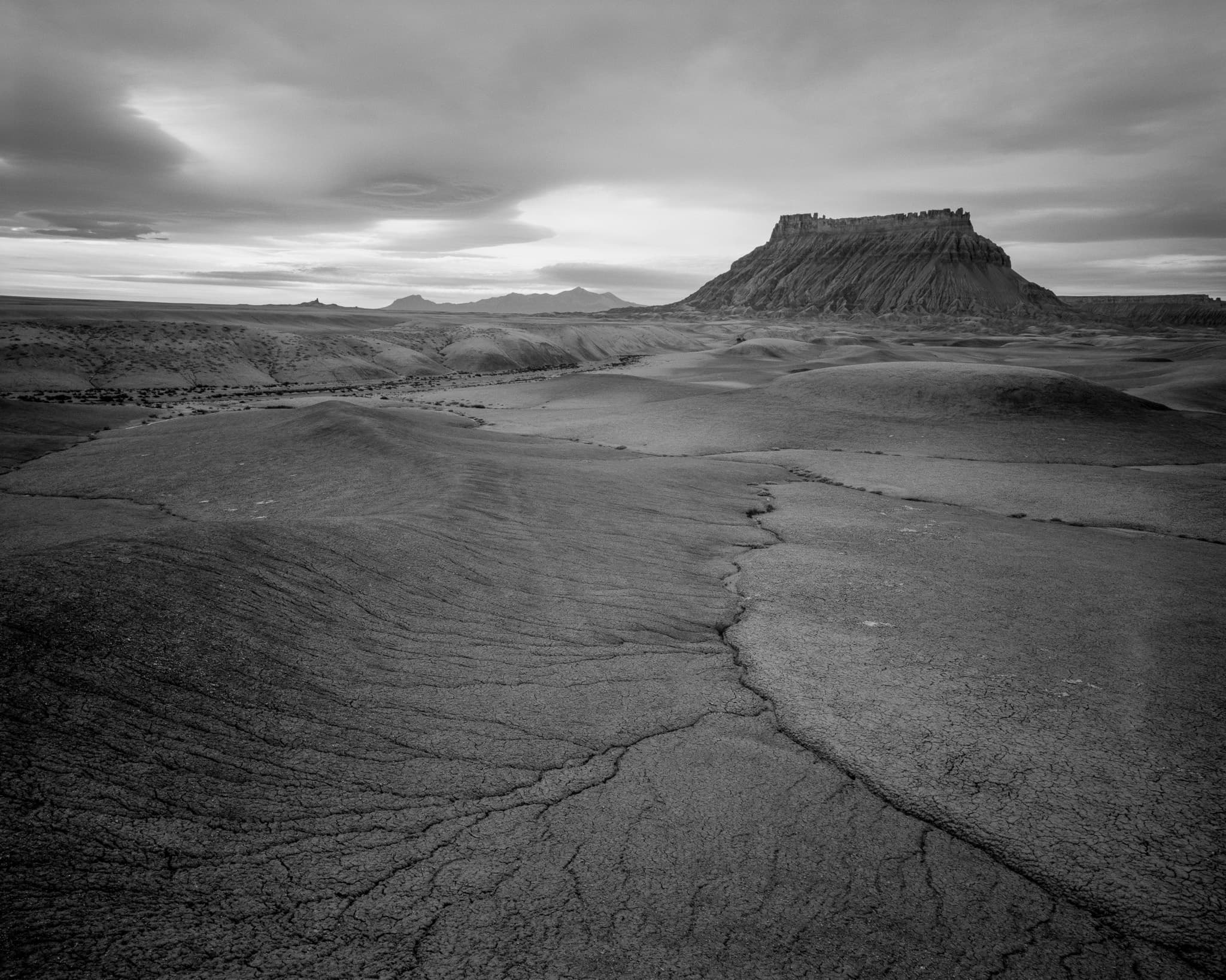 Factory Butte rises from the Utah badlands under a completely overcast sky — no blue, no direct sun, just flat light and leading lines pointing toward the butte. Photograph by Marty Quinn