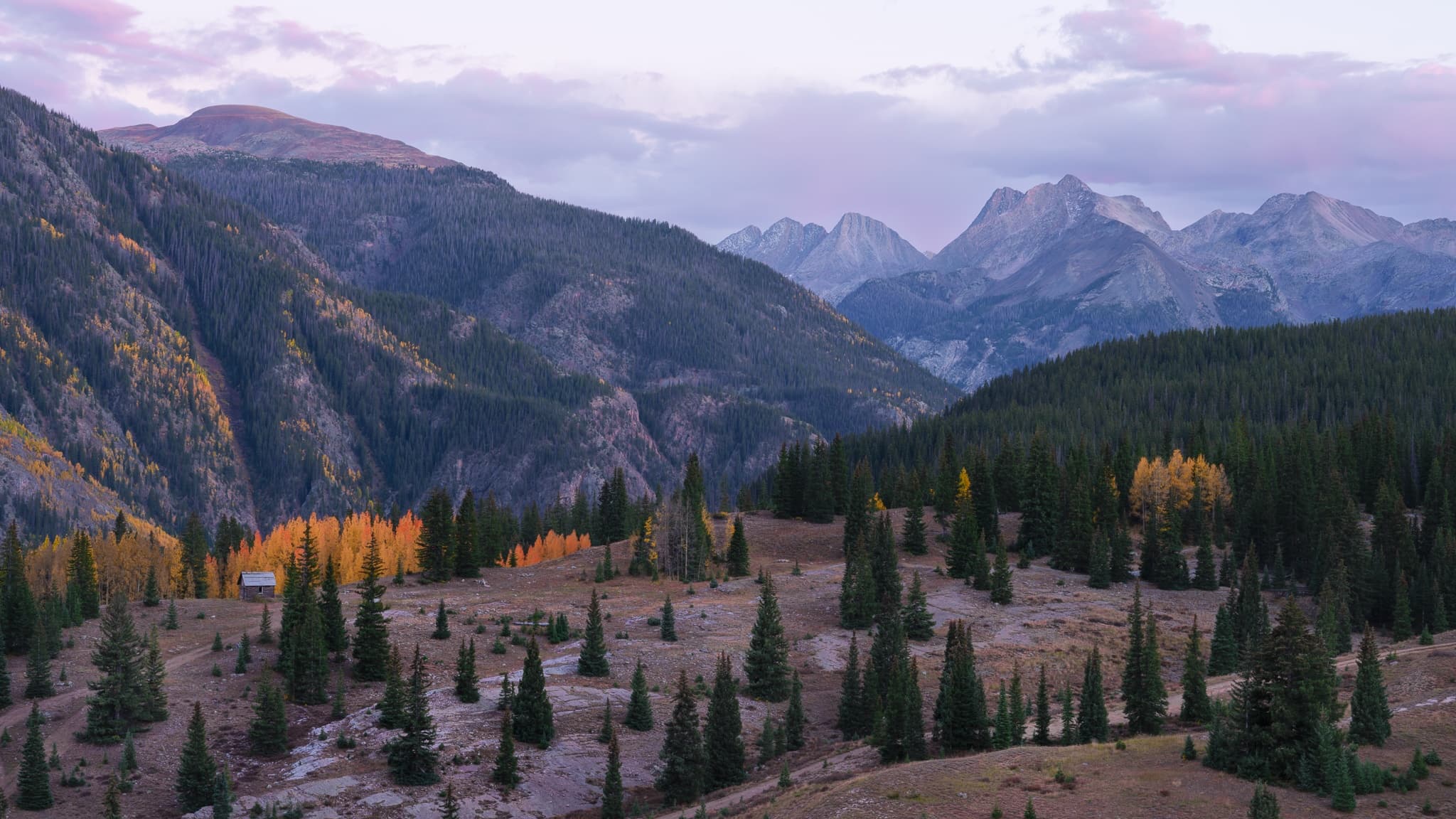 A small mountain cabin at the edge of fall color in the Colorado Rockies, caught at sunset with the peaks behind it going orange. Photograph by Marty Quinn