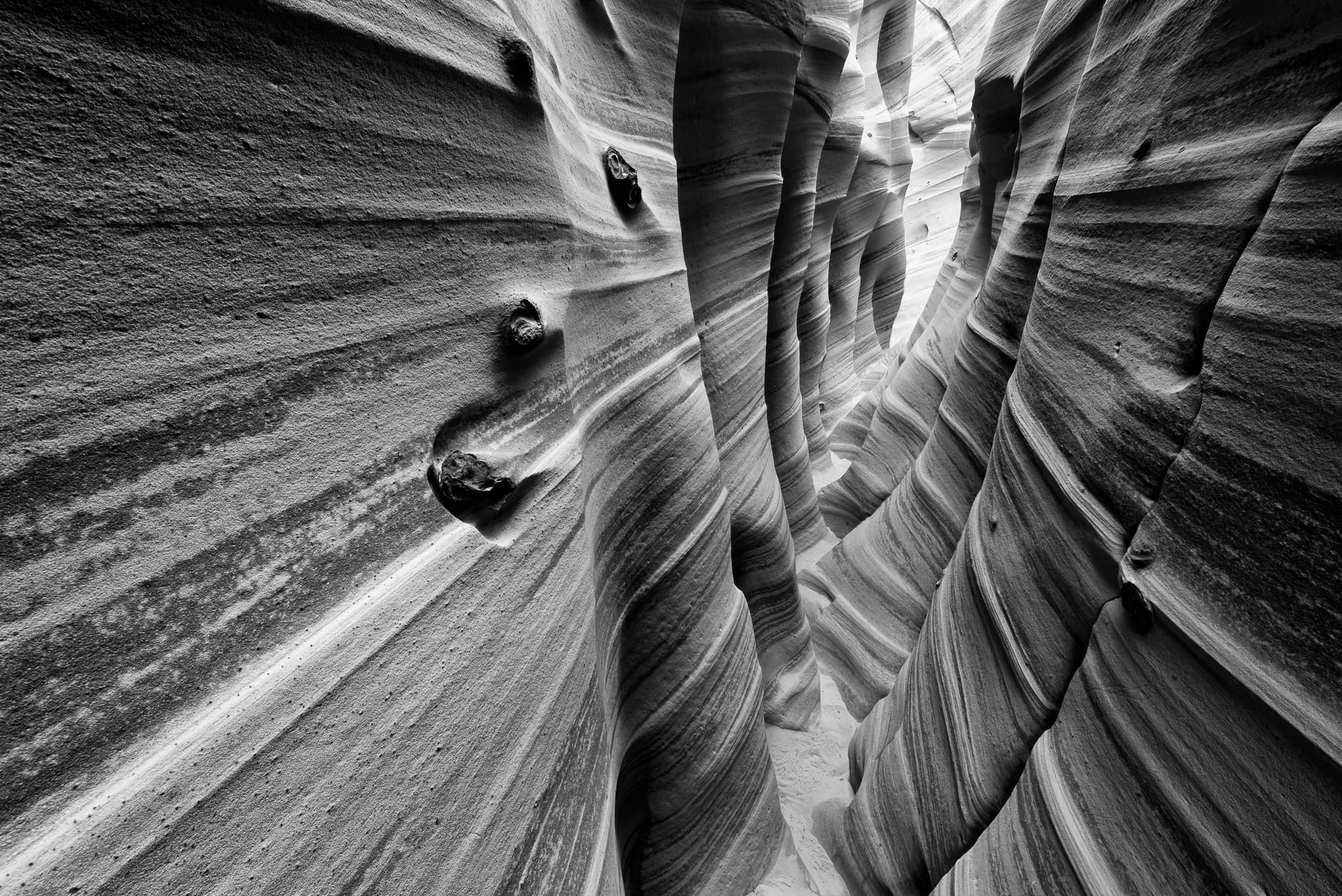 Diagonal bands of cross-bedded Navajo sandstone line the walls of a Utah slot canyon in this black and white study of layered rock and narrow light. Photograph by Marty Quinn