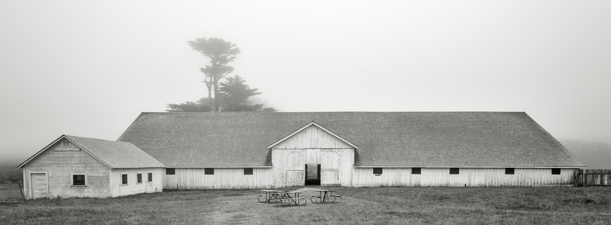 A large hay barn emerges from morning fog in the rural American countryside, California. Photograph by Marty Quinn