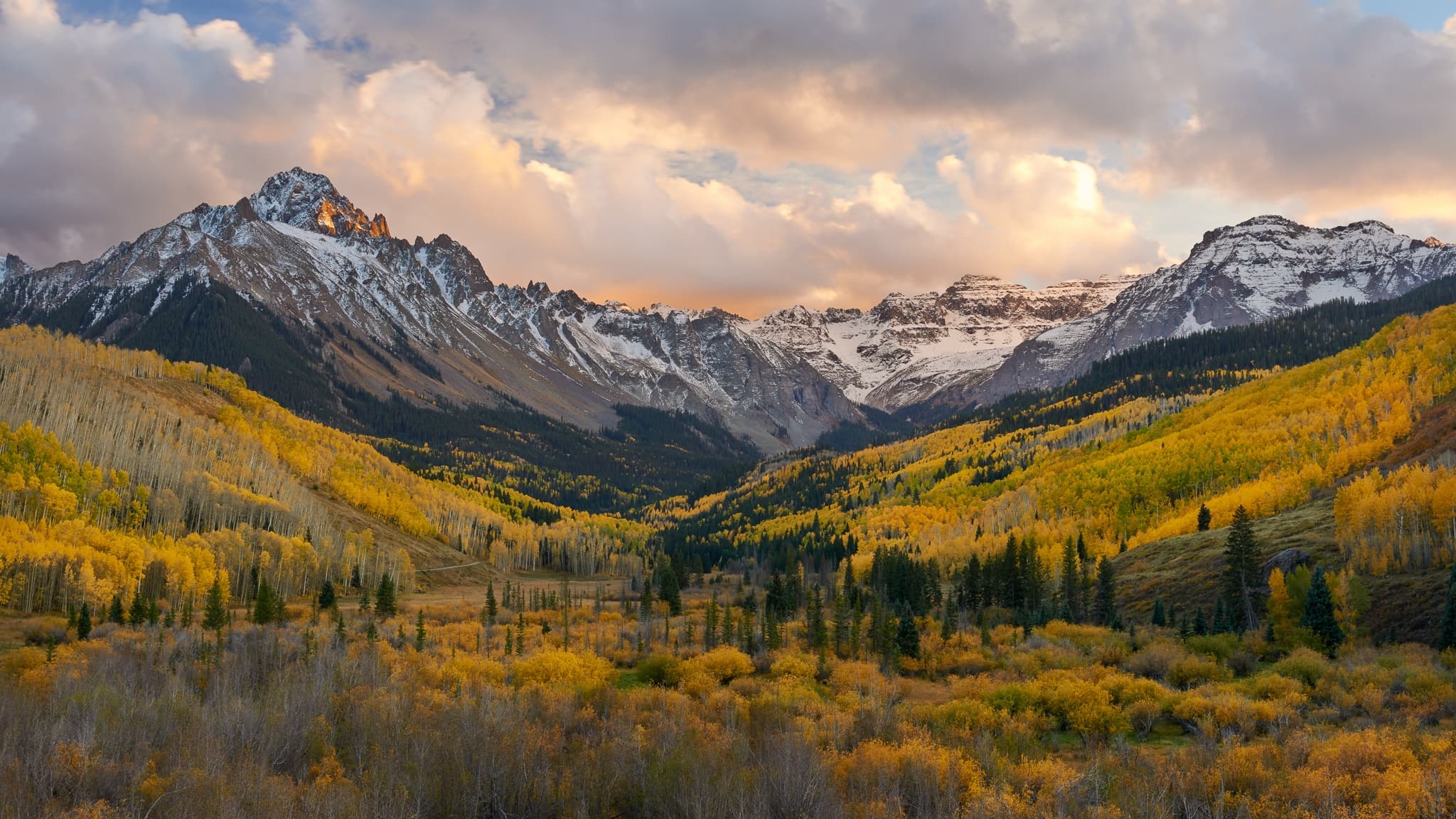 Sunset light ignites golden aspen hillsides below the snow-dusted Sneffels Range in Colorado's San Juan Mountains. Photograph by Marty Quinn