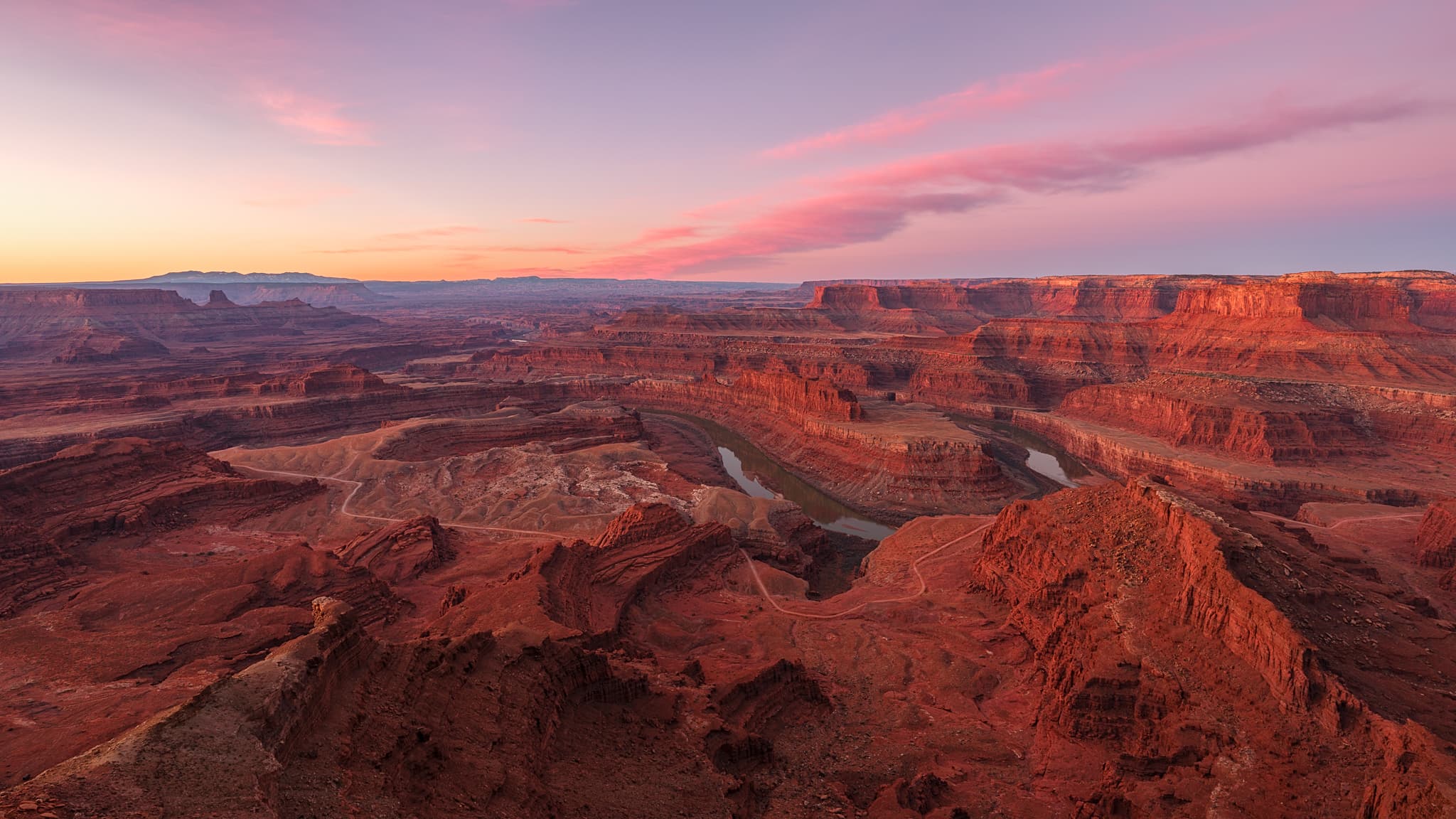 Dead Horse Point, Utah: the Colorado River loops 2,000 feet below the overlook as first light turns the canyon walls copper and pink clouds drift over Canyonlands. Photograph by Marty Quinn